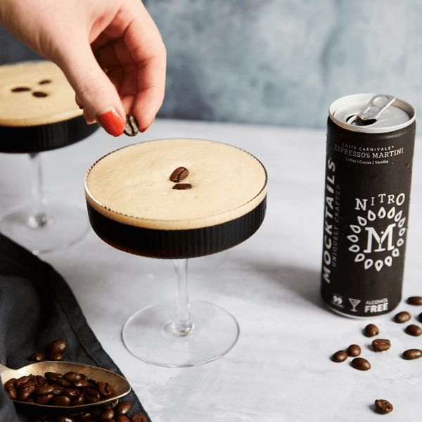 Hand garnishing a non-alcoholic espresso martini beside Nitro Mocktails Espress0% Martini can—smooth, alcohol-free coffee cocktail.