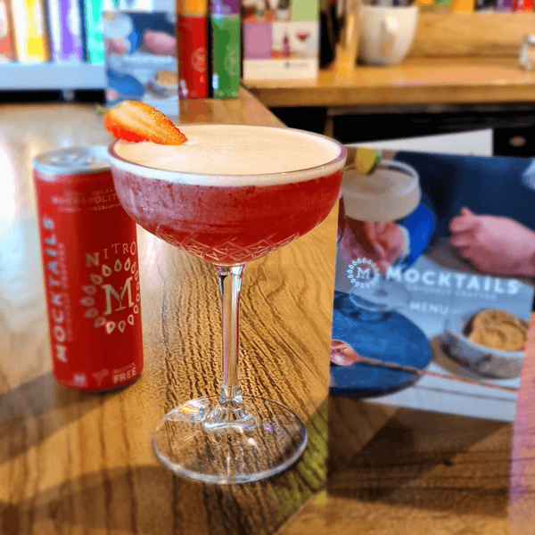 Served Mockapolitan cosmopolitan mocktail with strawberry garnish and brand menu on a bar countertop.