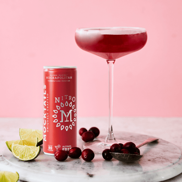 Mockapolitan can beside a cranberry and lime cosmopolitan in a cocktail glass on a pink background.