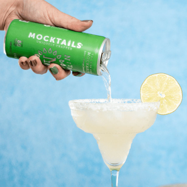 Hand pouring Nitro Mocktails Mockarita into a salt-rimmed margarita glass with lime—smooth, nitro-infused alcohol-free cocktail.
