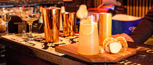 Bar setup featuring non-alcoholic Nitro Mocktails Mockscow Mule can served in glassware and bar tools on a wooden cutting board.